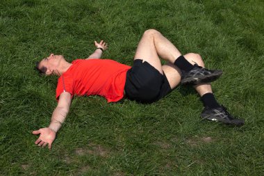 Man exercising resting and stretching on grass in the sunshine clipart