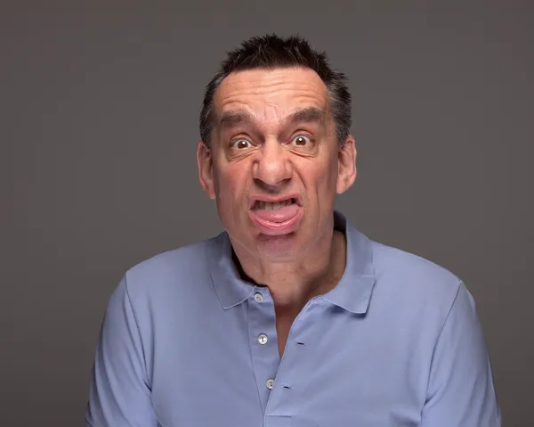 Mann zieht Gesicht herausstreckende Zunge auf grauem Hintergrund Stockfoto