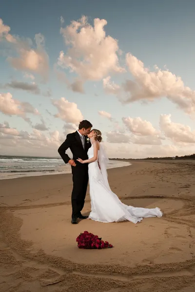 Жених и невеста целуются в песчаном сердце любви — стоковое фото