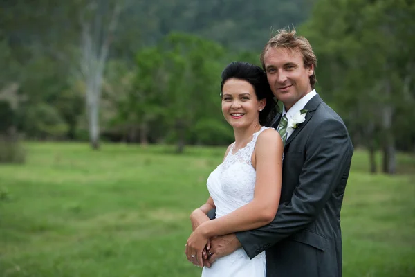 Bruid en bruidegom knuffelen in een groen veld — Stockfoto