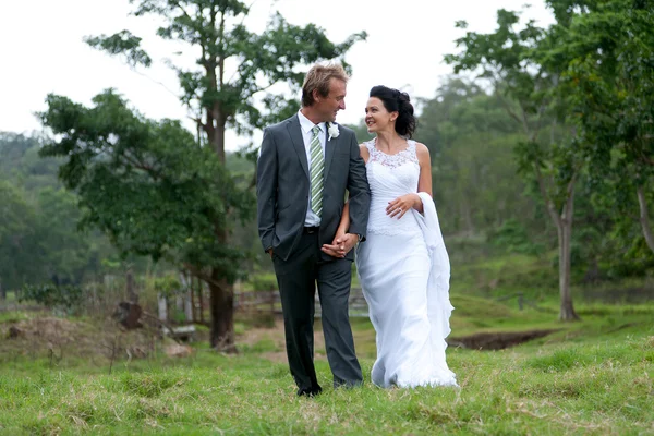 Bruid en bruidegom lopen hand in hand in landelijke omgeving — Stockfoto