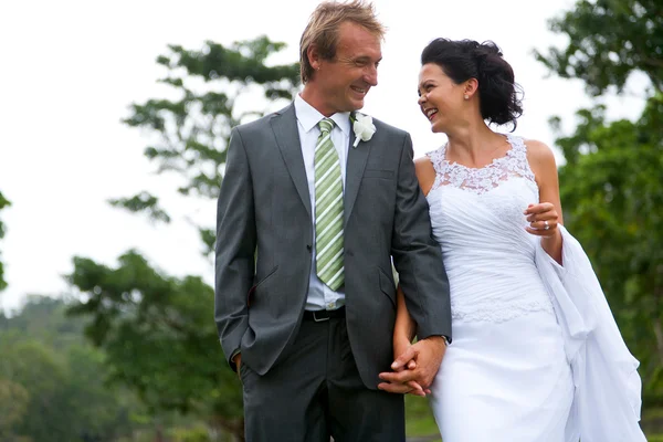 Noiva e noivo andando de mãos dadas em um ambiente rural — Fotografia de Stock