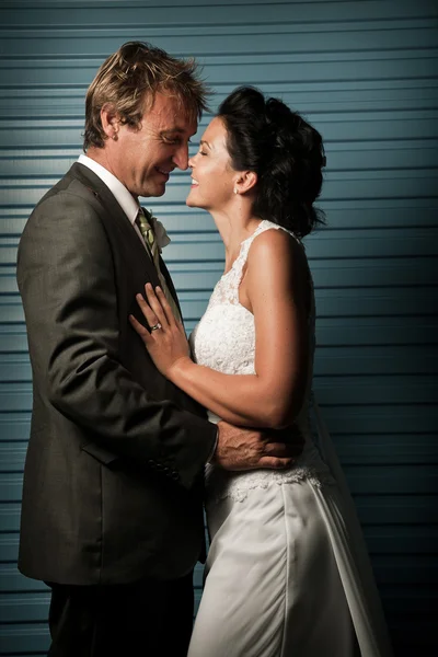 Noiva e noivo tocando narizes contra uma parede azul — Fotografia de Stock