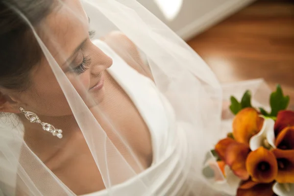 Bela noiva olhando através de seu véu em seu buquê — Fotografia de Stock