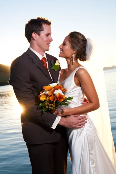 Groom holding bride at sunset with sunburst — Stock Photo, Image