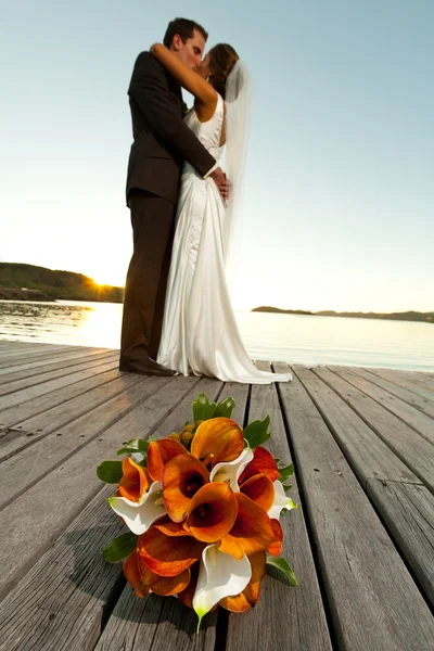 Bruiloft boeket in voorgrond en pasgetrouwden achter — Stockfoto