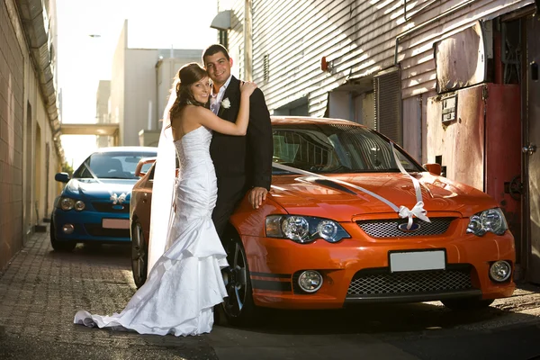 Recién casados abrazándose en un callejón con coches de boda —  Fotos de Stock