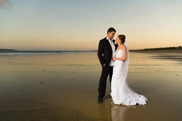 Newlyweds on a deserted beach at sunset — Stock Photo, Image