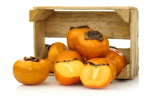 Verse kaki fruit en een verlaging van één in een houten krat — Stockfoto