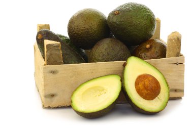 Fresh and ripe avocado's and a cut one in a wooden crate clipart