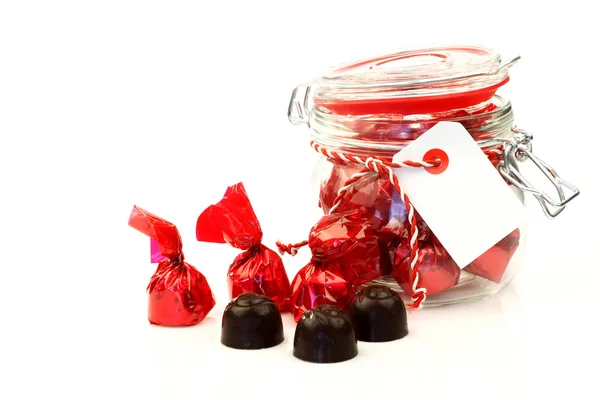 Un frasco de vidrio lleno de deliciosos bombones envueltos en papel rojo brillante —  Fotos de Stock
