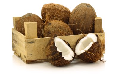 Fresh coconuts and a cut one in a wooden crate clipart