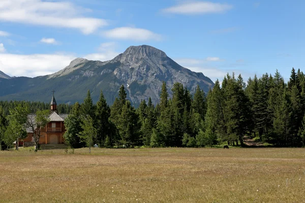 Petite église en bois rouge à travers une plaine contre la forêt, moun rocheux — Photo