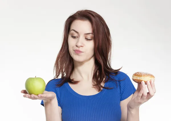 Junge Frau hat die Wahl zwischen Apfel und Donut lizenzfreie Stockfotos