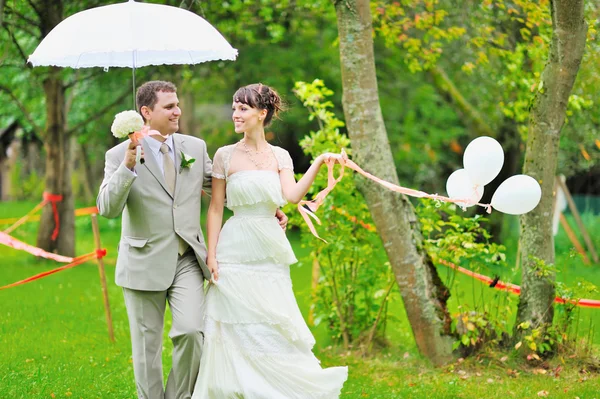 Happy bride and groom walking together in a park — Stock Photo, Image