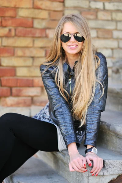 Verbluffend mooie jonge blonde vrouw in een jas en vlieger zonnebril zittend op de trap — Stockfoto