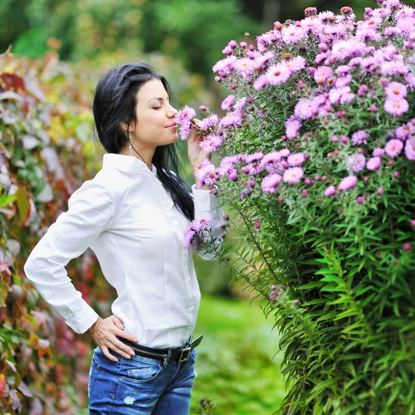 stock image Beautiful youg woman smelling flowers in a garden