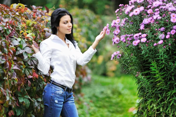 Hermosa mujer joven mirando flores en un jardín —  Fotos de Stock