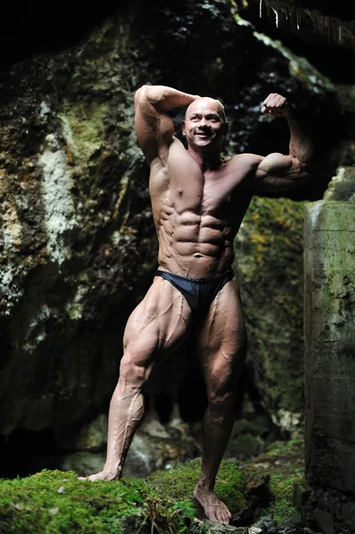 Giovane bodybuilder in posa in una grotta - Vista frontale — Foto Stock