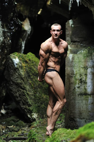 Bodybuilder poseren in een grot — Stockfoto