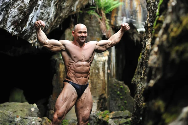 Bodybuilder posing in a cave — Stock Photo, Image