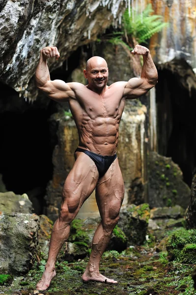 Giovane bodybuilder in posa in una grotta - Vista frontale — Foto Stock