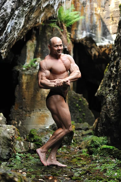 Unga bodybuilder poserar i en grotta - full längd porträtt — Stockfoto