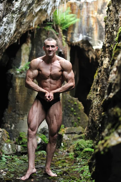 Bodybuilder posing in a cave — Stock Photo, Image