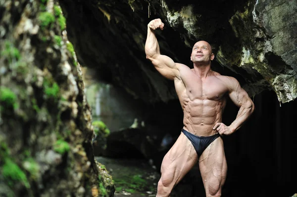 Giovane bodybuilder in posa in una grotta — Foto Stock