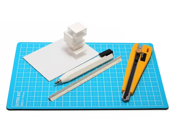 Cortador, lápis, escala e modelo arquitetônico colocado sobre cutti azul — Fotografia de Stock