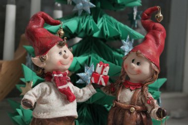 Christmas elfs boy and girl giving a present under christmas tre clipart