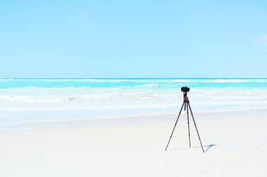 Digital Camera and tripod on white beach for landscape photograp clipart