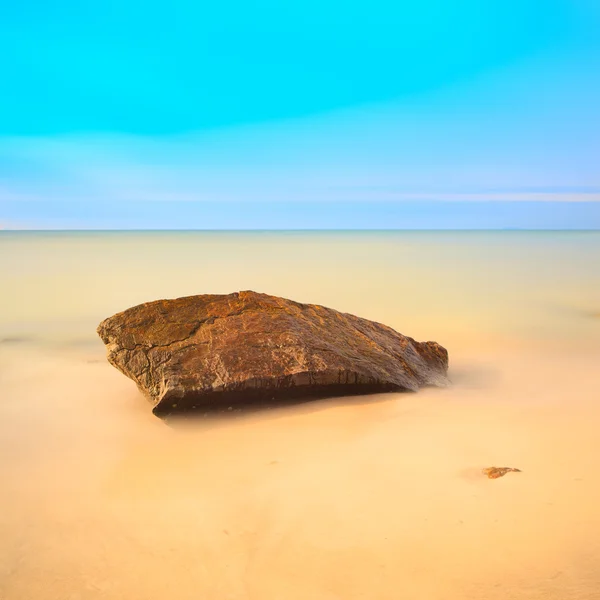 Platte rots op een gouden strand. lange blootstelling. — Stockfoto