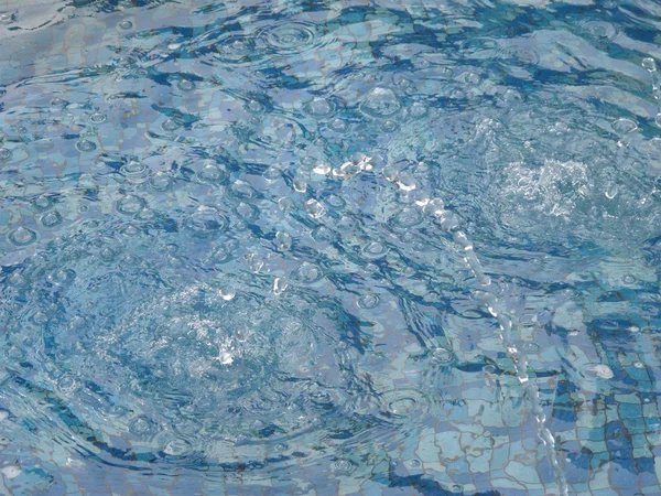 Волны от капель на голубой воде бассейна — стоковое фото
