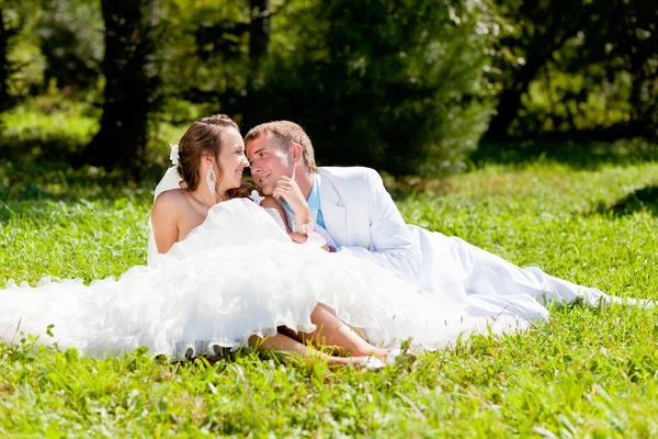 Bruden och brudgummen kramas sittande på grönt gräs — Stockfoto