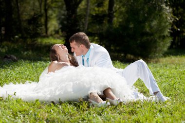 Bride and groom huggling sitting at green grass clipart