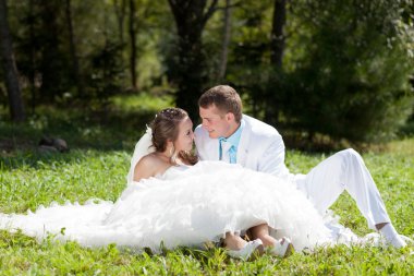 Bride and groom huggling sitting at green grass clipart