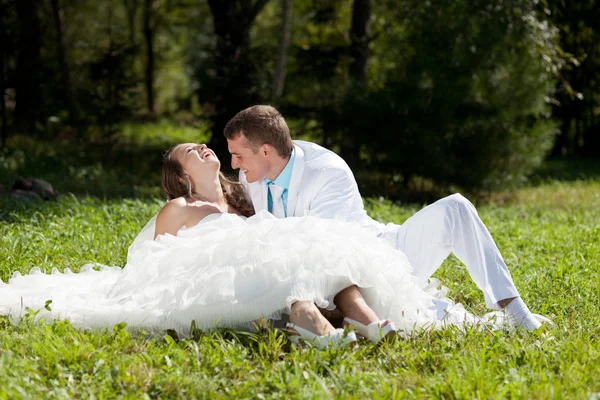 Gelin ve damat huggling yeşil çimlere oturup — Stok fotoğraf