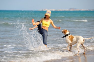 genç kadın köpeğiyle kumsalda oynarken