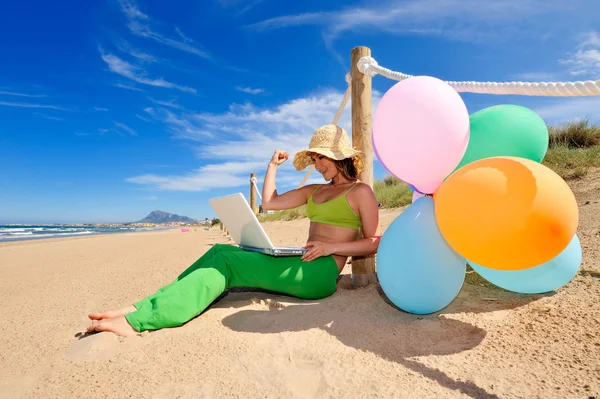 Женщина с красочными воздушными шарами с помощью ноутбука на пляже — стоковое фото