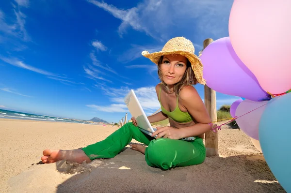 Frau mit bunten Luftballons mit Laptop am Strand — Stockfoto