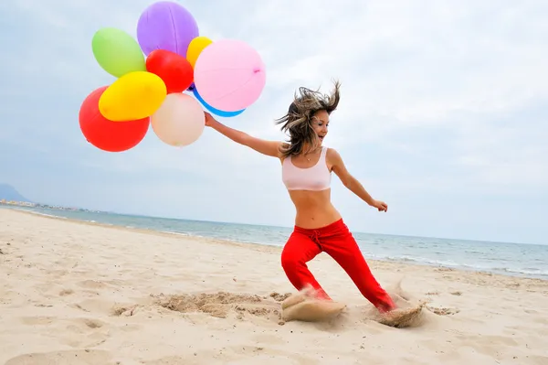 Mladá žena s barevnými balónky na pláži — Stock fotografie