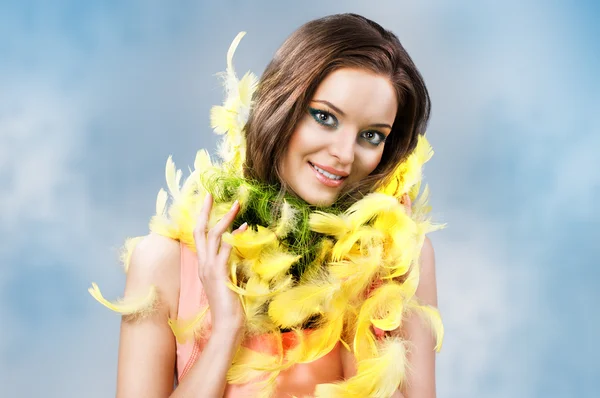 Easter picture of young woman with yellow feathers against blue sky background — Stock Photo, Image