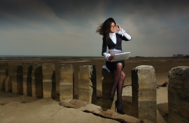 Business lady sitting on the beach, on a background cloudy sky. clipart