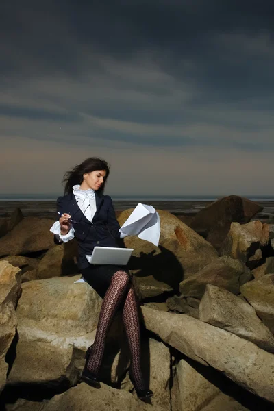 Femme d'affaires assise sur les rochers au bord de la mer, sur fond de ciel nuageux . — Photo