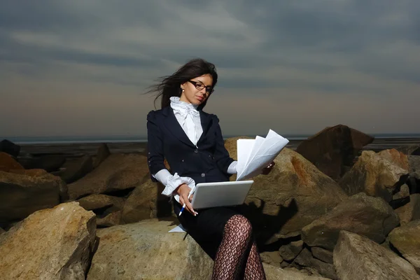 曇り空を背景に、海で岩の上に座っている女性のビジネス. — ストック写真
