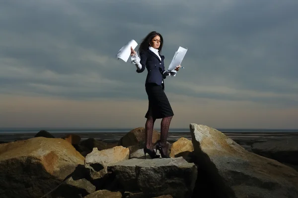 曇り空を背景に、海沿いの岩の上に立ってのビジネスの女性. — ストック写真
