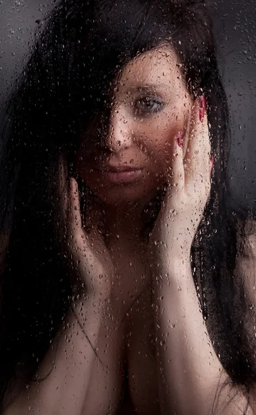 裸体女孩在黑色背景上淋湿的玻璃 — 图库照片