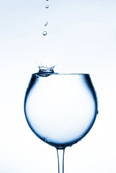 stock image A glass of clear liquid and a drop falling into it.