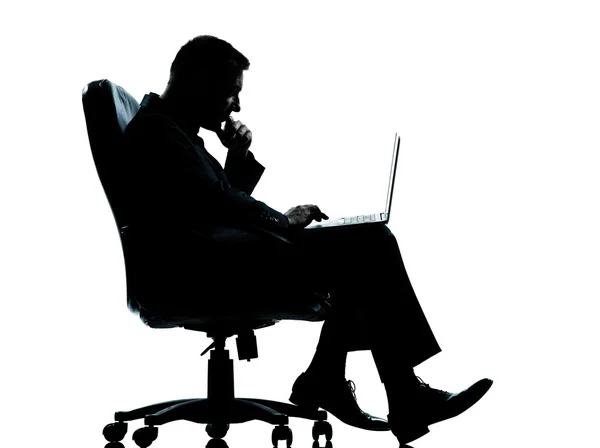 Um homem de negócios computação computacional sentado em silhueta poltrona — Fotografia de Stock